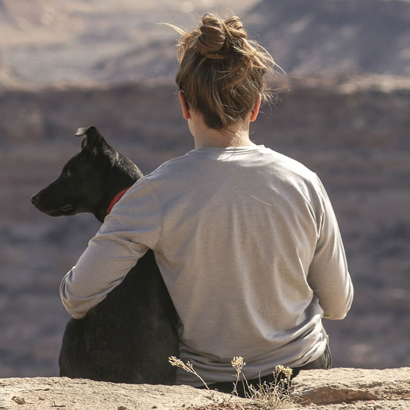 a girl and dog sitting on the ledge of a mountain